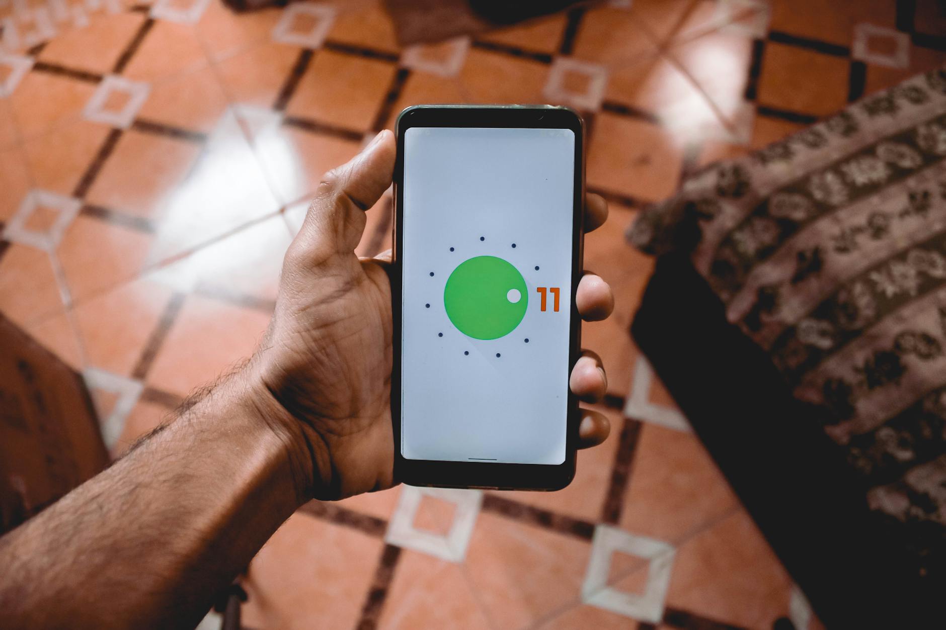 Malware na Androidzie: objawy infekcji i skuteczne czyszczenie Dłoń trzymająca smartfon z systemem Android 11 na tle wzorzystej podłogi