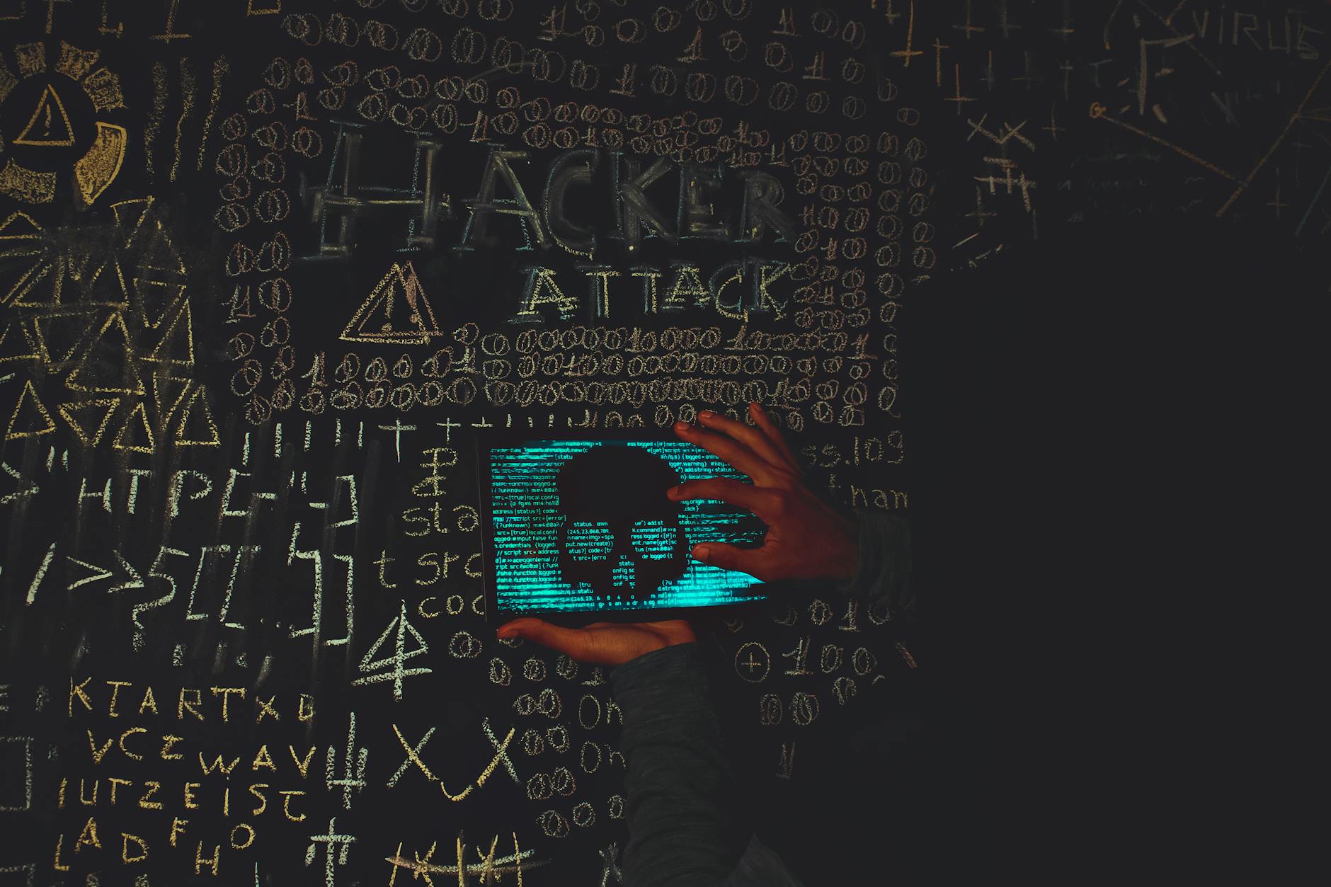 Haker w czarnej bluzie korzysta z tabletu z czaszką i napisem Hacker Attack