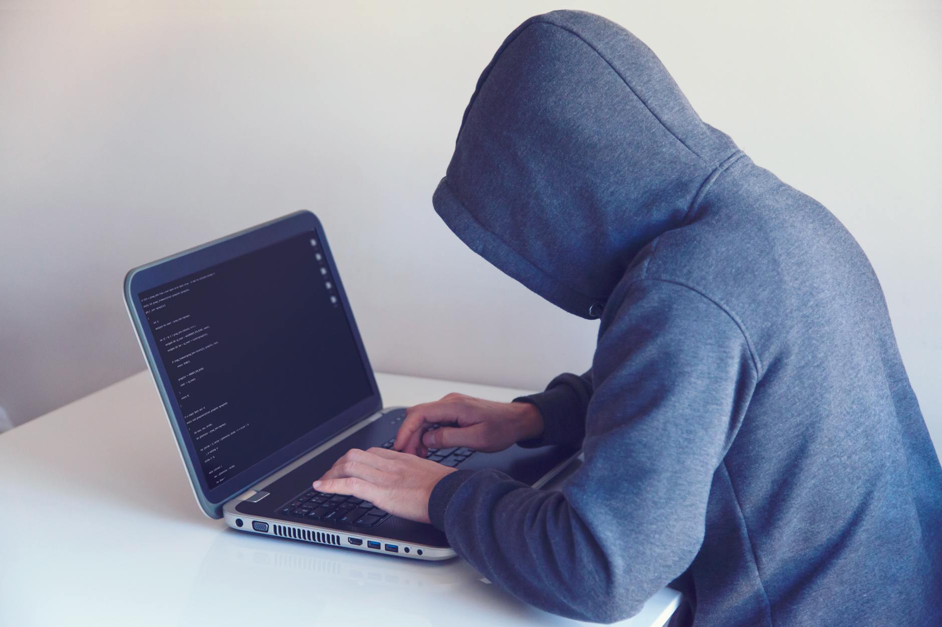 Haker w kapturze pracujący przy laptopie w jasnym pokoju